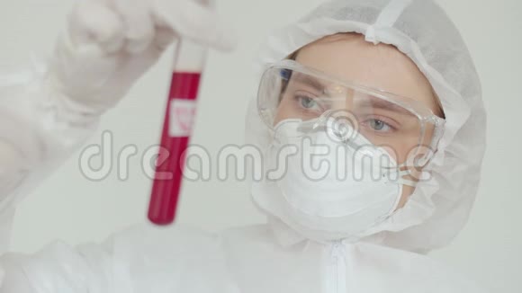 一位戴化学防护戴安全眼镜戴口罩的妇女检查一个红色试管一位年轻的女科学家在视频的预览图