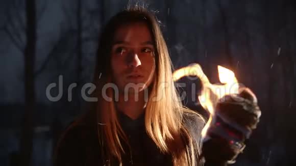 一位手持火炬的年轻女子站在冬天的森林里下着雪看着镜头视频的预览图