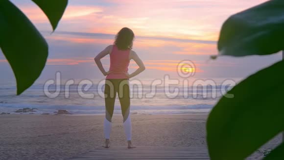 在海边穿着健身服的女人在日落时分做伸展运动视频的预览图