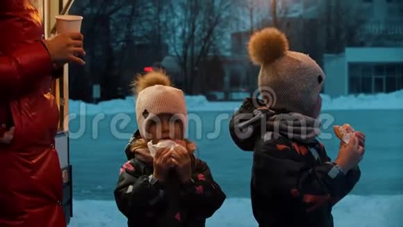一个年轻的女人和她的孩子一起喝热饮料和吃甜甜圈在冬天散步视频的预览图