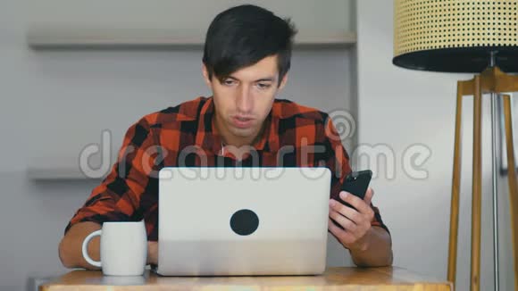自信忙碌的商人自由职业者在笔记本电脑上工作一边喝咖啡一边使用智能手机视频的预览图
