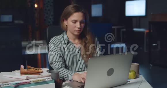 前景看到漂亮的女办公室工作人员在她的笔记本电脑上打字深夜年轻女子用她的电脑视频的预览图