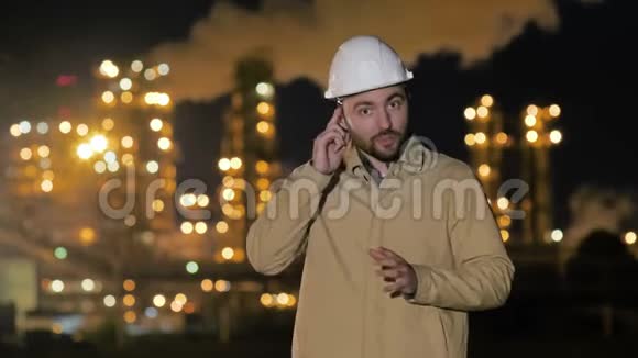年轻的工程师戴着白色的安全帽向站在工厂旁边的照相机解释一些事情视频的预览图
