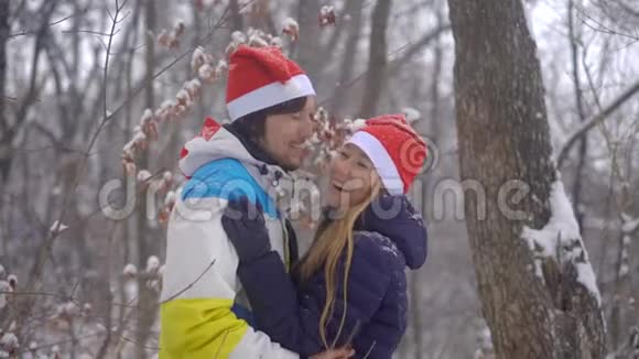 戴着红帽子的快乐年轻夫妇站在雪地里笑着接吻视频的预览图