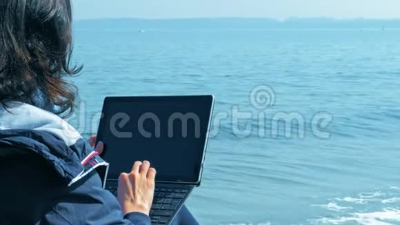 自由生活方式女人坐在海边用笔记本电脑视频的预览图