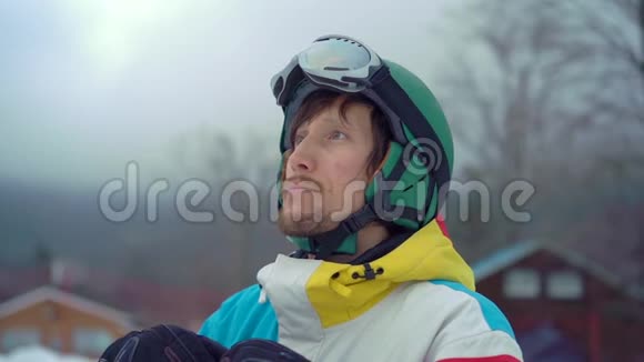 一个年轻人戴着头盔在一个山区度假胜地用滑雪板拍摄的特写镜头他戴上他的雪谷歌冬季视频的预览图