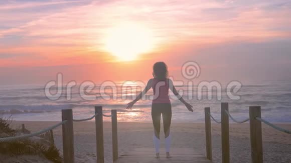 在日落时分穿着健身服的女人在海边的木步道上做瑜伽视频的预览图