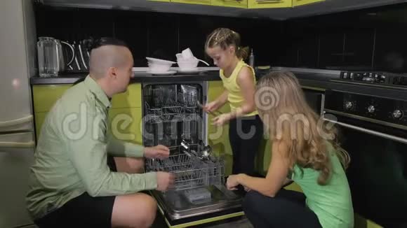 母亲和父亲教女儿学习使用洗碗机女主人把脏盘子装进去视频的预览图