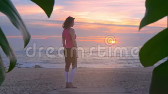 女人在海边的木制走道上做瑜伽美丽的夏日日落视频的预览图