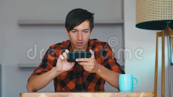 年轻人在家里用手机玩电子游戏男性在游戏过程中表现出不同的情绪视频的预览图