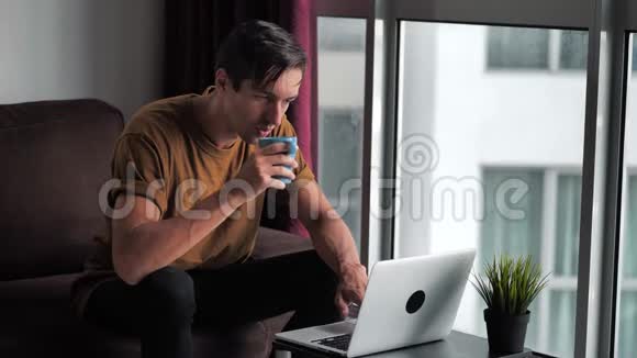 帅哥用笔记本电脑早上喝咖啡然后坐在家门口的沙发上视频的预览图