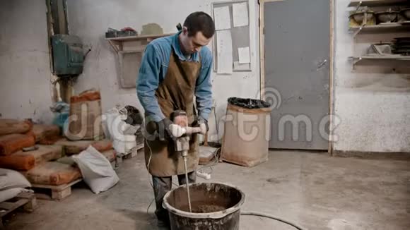 混凝土行业青年工人用手搅拌机将混凝土从水泥水和玻璃碎片中搅拌出来视频的预览图