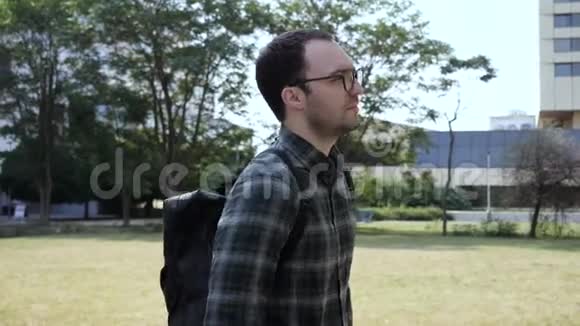 一个英俊的年轻人戴着眼镜和背包沿着公园散步视频的预览图