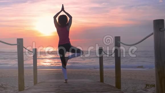 女子在木制沙滩步道练习瑜伽美丽的夏日日落视频的预览图