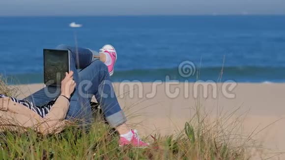 自由职业者女人躺在沙滩上在笔记本上工作视频的预览图