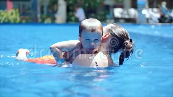 可爱的小男孩和他的母亲在游泳池里上游泳课妈妈或保姆教练握着她儿子的手视频的预览图