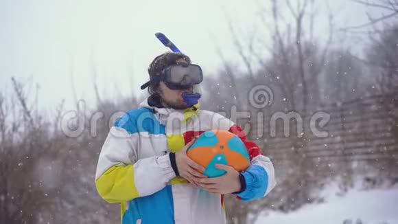 穿着带充气球的潜水面具的滑稽男子站在降雪下失去了时间视频的预览图