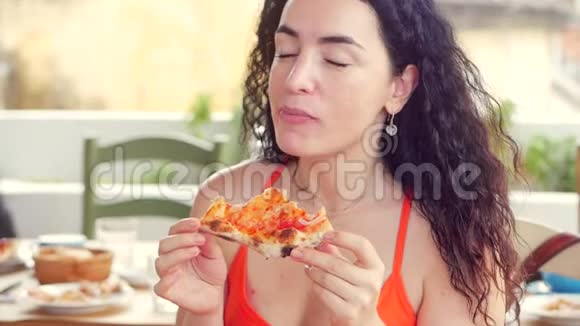 年轻可爱的意大利女人穿着红色连衣裙在餐馆里急切地吃和享受意大利披萨这就是视频的预览图