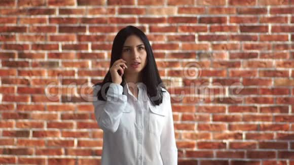 那个女孩在打电话一位年轻女子在智能手机上靠砖墙交流视频的预览图