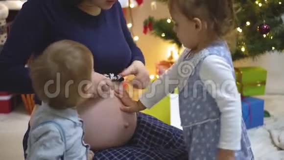 两个孩子摸索着倾听亲吻怀孕母亲的肚子视频的预览图