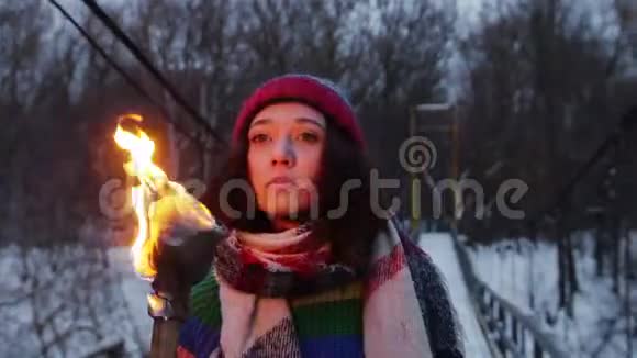 一个年轻的女人在森林里的雪桥上走着手里拿着燃烧的火炬环顾四周视频的预览图