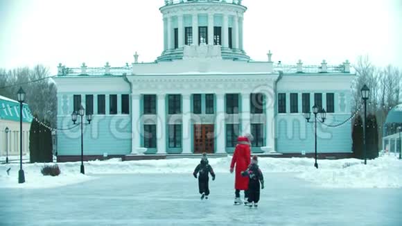 一个年轻的家庭母亲和两个孩子在公共溜冰场上滑冰背景是某栋建筑视频的预览图