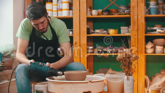 陶器穿绿色t恤的主人正在用建筑吹风机烘干粘土碗视频的预览图