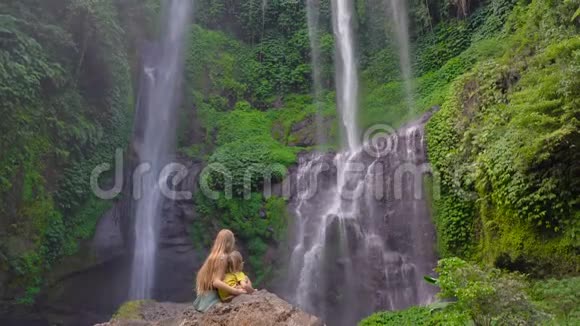 年轻女子和她的小儿子游客参观巴厘岛上最大的瀑布塞库普尔瀑布旅费视频的预览图