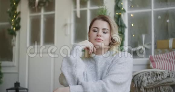 穿着温暖毛衣的欧洲年轻迷人女子坐在斯堪的纳维亚内部看着相机舒适视频的预览图