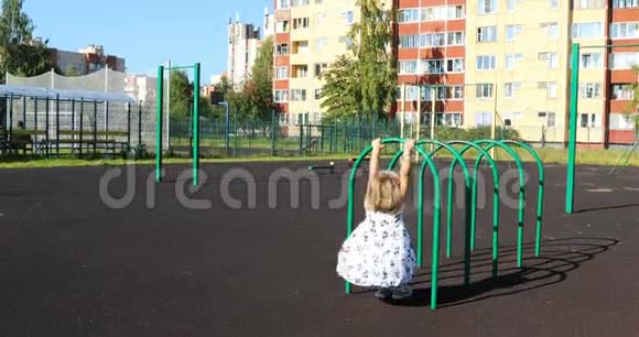 四岁的金发女孩穿着一件蓬松的白色连衣裙在体育场的水平杆上练习视频的预览图