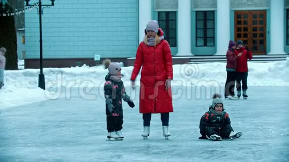 一位年轻的母亲穿着红色羽绒服和她的孩子们在冰上滑冰视频的预览图