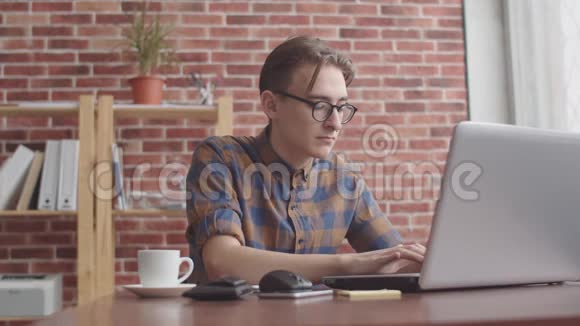 这位自由职业者正在笔记本电脑上打字喝着咖啡对着相机微笑一个穿鼻子的嬉皮士视频的预览图