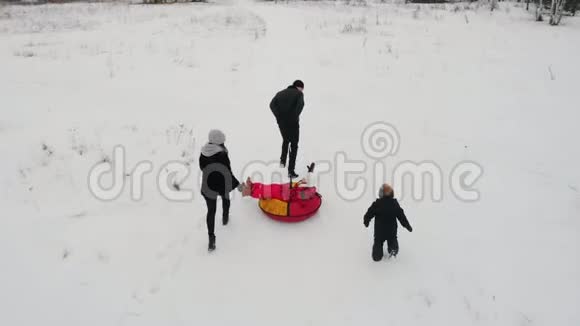 一家人在冬天的田野上玩耍父亲骑着儿子的充气雪橇他的妻子和女儿追赶视频的预览图