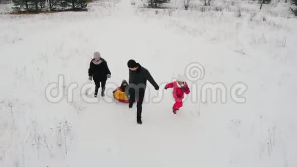 一家人在冬天的田野上玩耍父亲骑着儿子在充气雪橇上他的妻子和女儿在附近跑步视频的预览图
