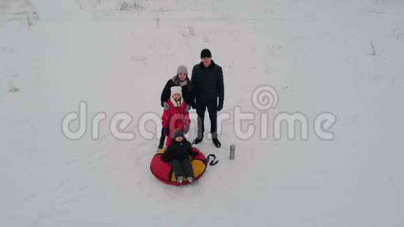 一家人站在雪域的中间小男孩坐在充气雪橇上视频的预览图
