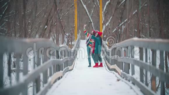 两个穿着五颜六色衣服的年轻女性朋友在电话里自拍站在雪桥上视频的预览图