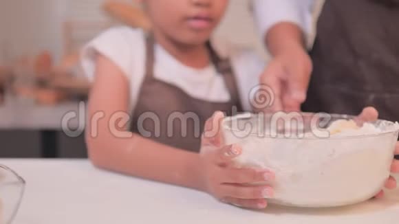 小亚洲女孩和妈妈帮助把碗里的面粉混合在一起做了一个自制的面包店视频的预览图
