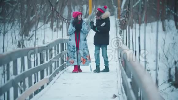 两个女人走在森林里的雪桥上喝着热水瓶里的热饮视频的预览图