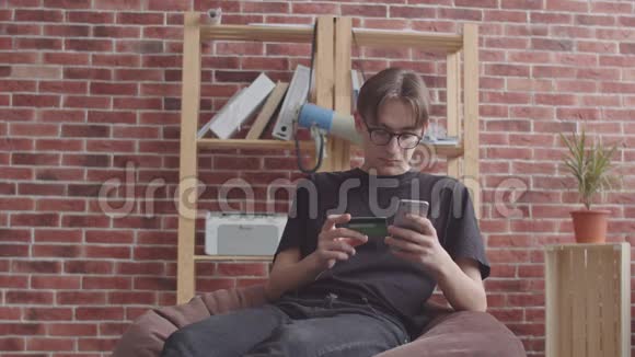 一个瘦小的家伙坐在包椅上用银行卡在网上商店买东西一个有鼻子的嬉皮士视频的预览图
