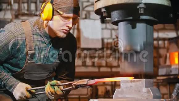 眼镜上的铁匠在锻造机的压力下放置较长的金属片视频的预览图
