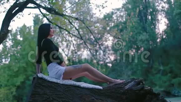 性感年轻的黑发女人坐在倒下的树干上远远地看着视频的预览图