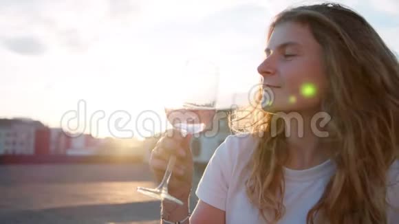 年轻女子在屋顶日落时喝玫瑰酒视频的预览图