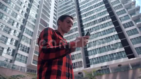年轻人在住宅摩天大楼高层建筑的背景下使用智能手机视频的预览图