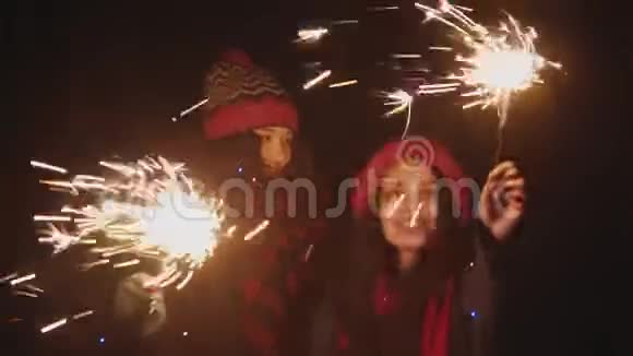 两个微笑的年轻女人晚上在户外玩火花灯看着镜头视频的预览图