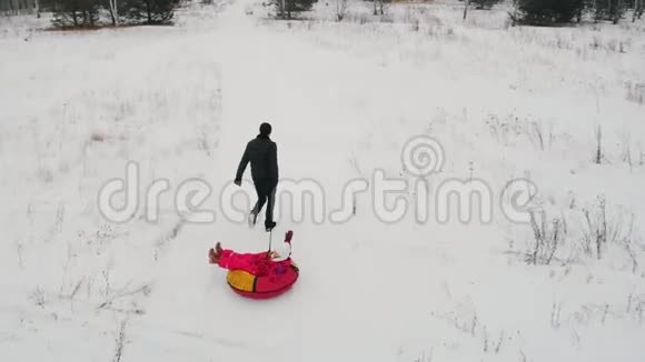 快乐的一家人在冬天的田野上玩耍父亲骑着他的儿子在充气雪橇上他的妻子和女儿在跑步视频的预览图