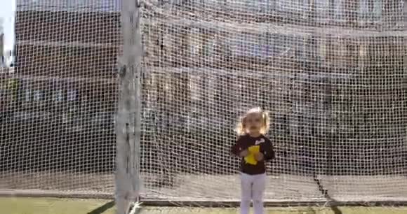 一个浅头发的女孩拿着一个软玩具在足球球门的球场上玩耍视频的预览图