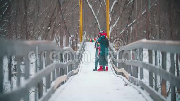两个穿着五颜六色衣服的年轻女朋友在雪桥上自拍视频的预览图