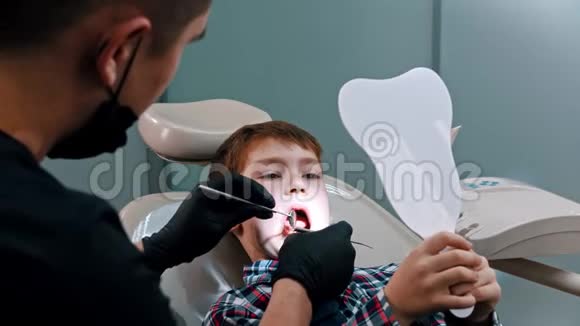 一个小男孩在现代牙科治疗男孩拿着镜子看在做什么牙医视频的预览图