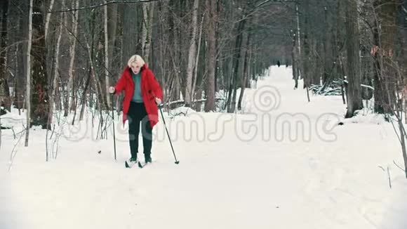 一个年轻的金发女人穿着红色羽绒服在森林里滑雪视频的预览图