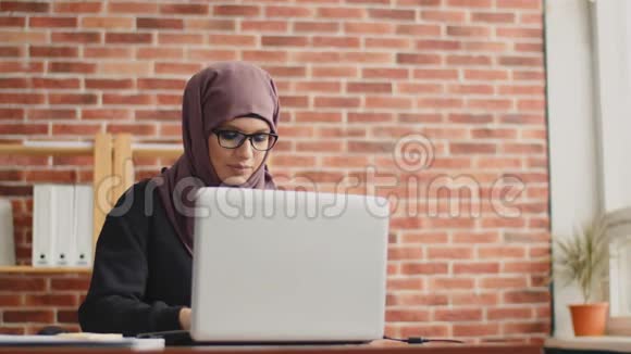 这名妇女是一名穆斯林办公室工作人员在笔记本电脑上打字戴头巾的女孩办公室概念视频的预览图